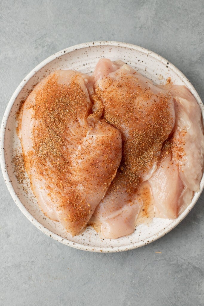A collage with step by step instructions showing how to make BBQ Chicken. Raw chicken breasts being seasoned with a dry rub