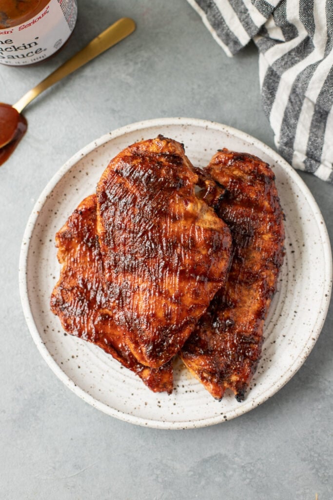 BBQ Chicken fresh off the grill on a white plate on a grey background