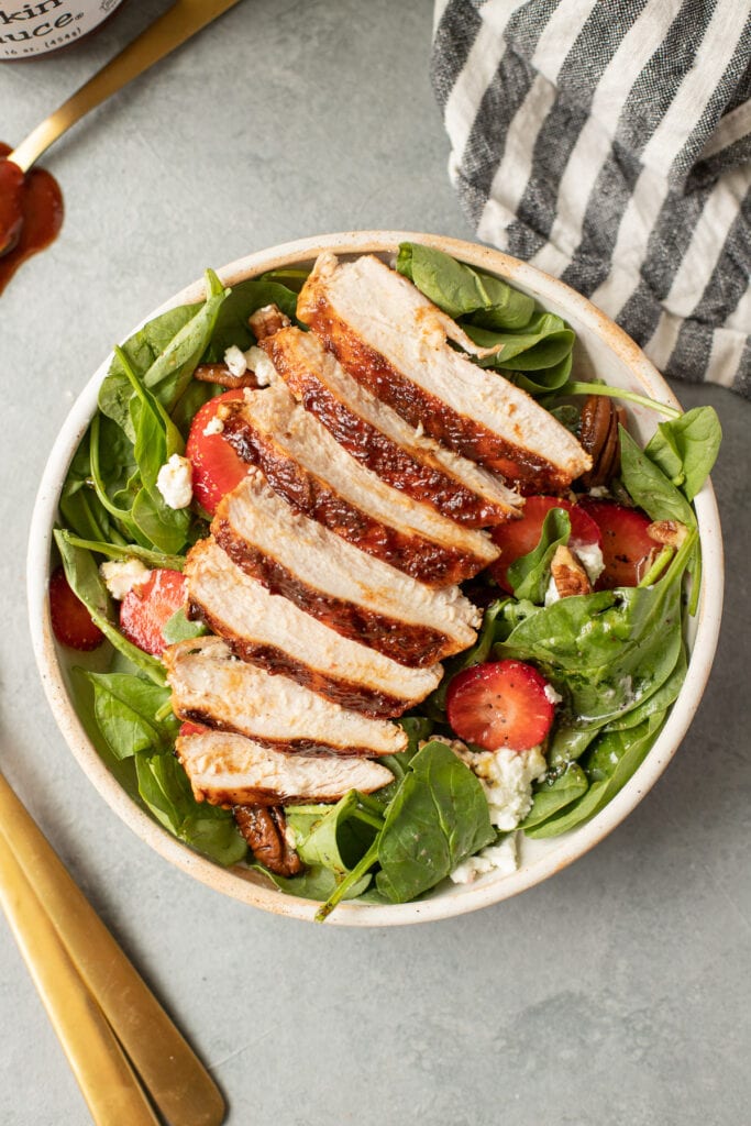 A close up of grilled BBQ Chicken Recipe sliced on a strawberry spinach salad
