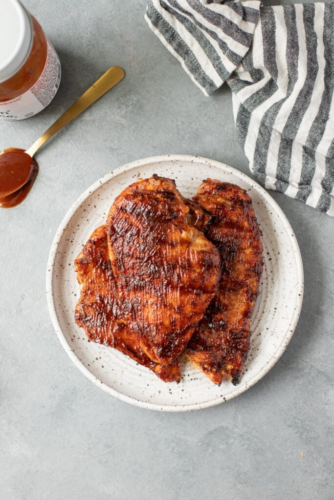 An overhead image of BBQ chicken on a white plate on a grey background
