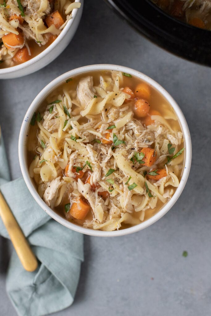 A big bowl of cozy chicken noodle soup made in the crockpot on a grey background