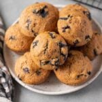 A close up of Healthy Blueberry Muffin Recipe on a white plate on a grey background with a striped linen off to the side