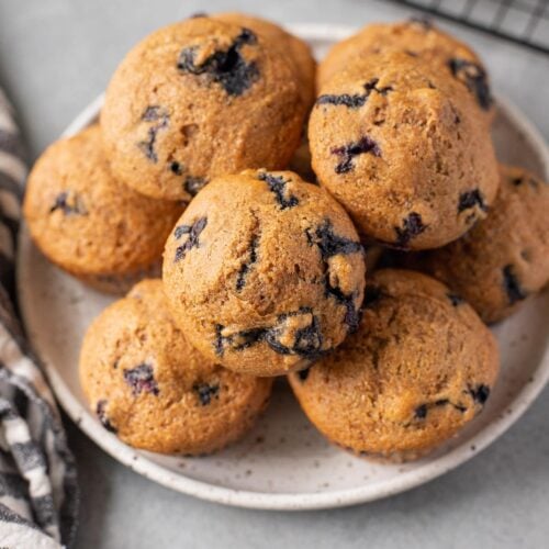 A close up of Healthy Blueberry Muffin Recipe on a white plate on a grey background with a striped linen off to the side