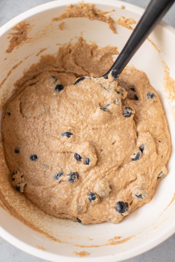 A bowl of blueberry muffin batter with a spatula stirring it together