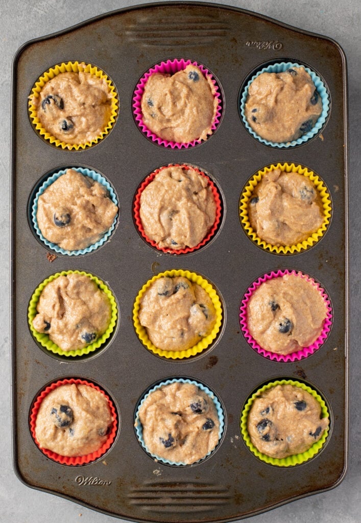 An overhead image of healthy blueberry muffins in a grey muffin tin filled with muffin batter