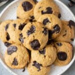 A close up of Healthy Chocolate Chip Cookies on a white plate with a linen and cookie sheet off to the side