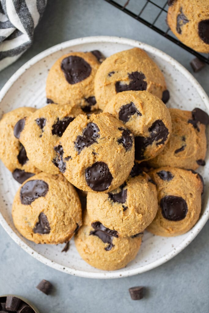 A close up of Healthy Chocolate Chip Cookies on a white plate with a linen and cookie sheet off to the side