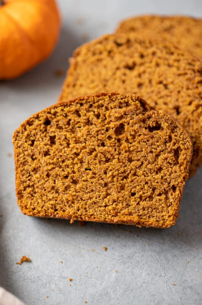 A close up of a slice of whole wheat pumpkin bread on a grey background