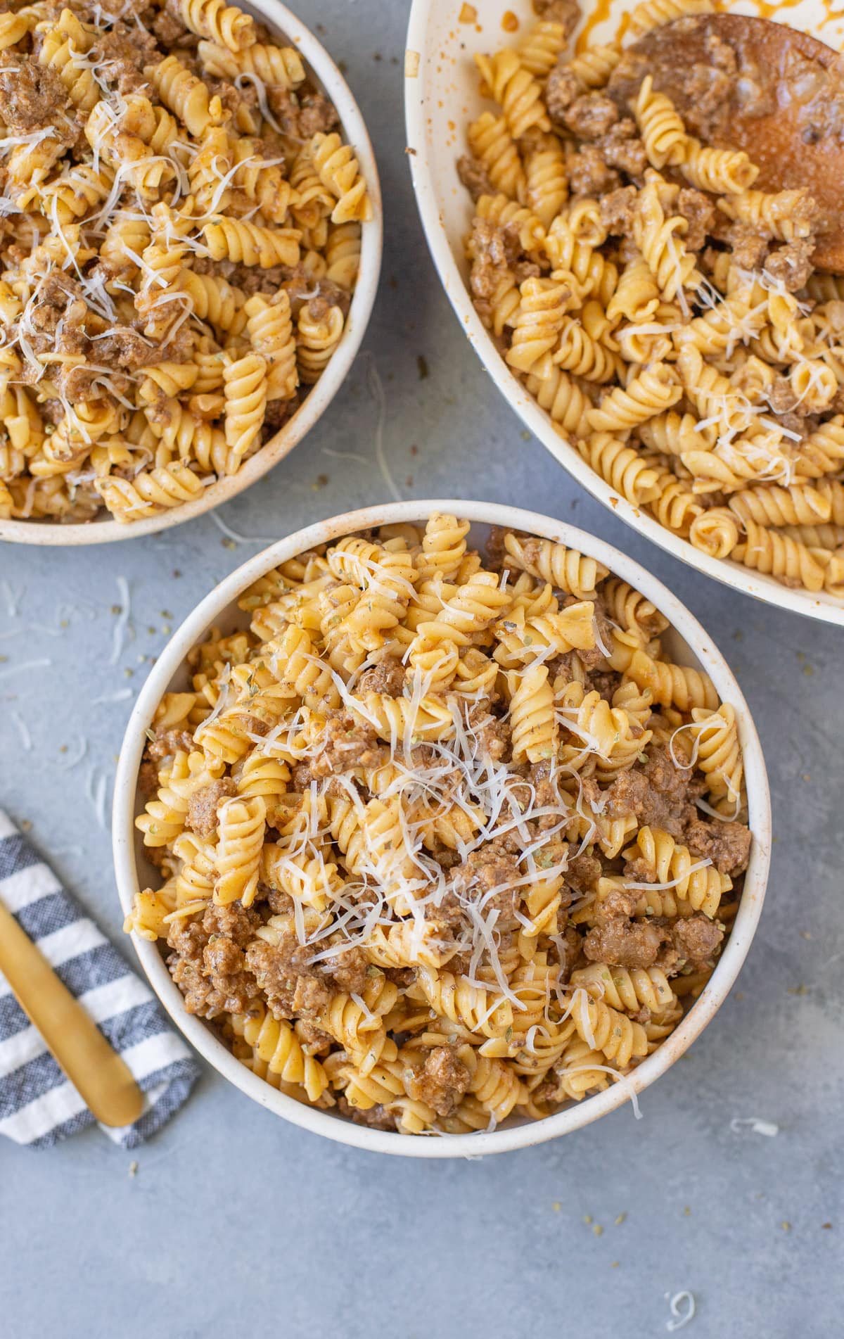 Two bowls and a skillet full of healthy hamburger helper made with rotini pasta, lean ground beef and shredded cheese.