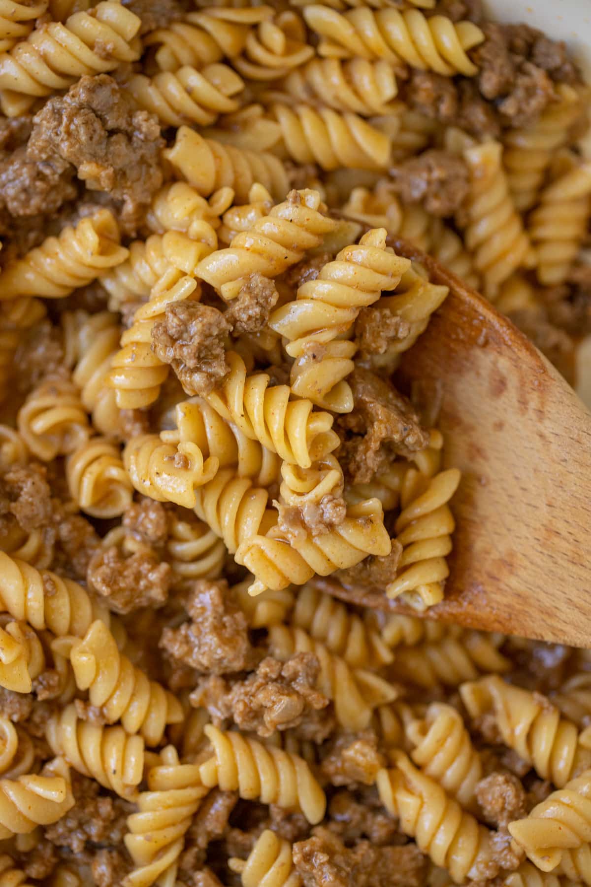 A close up of homemade hamburger helper being scooped up with a wooden spoon.