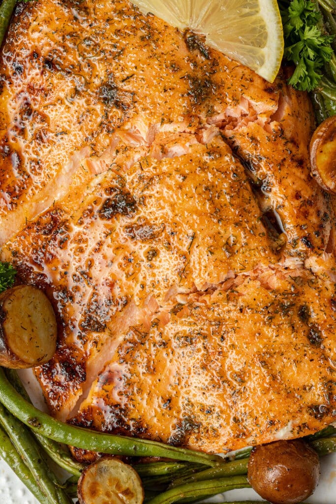 A close up of lemon salmon on a sheet pan with green beans, potatoes and lemon slices on the side