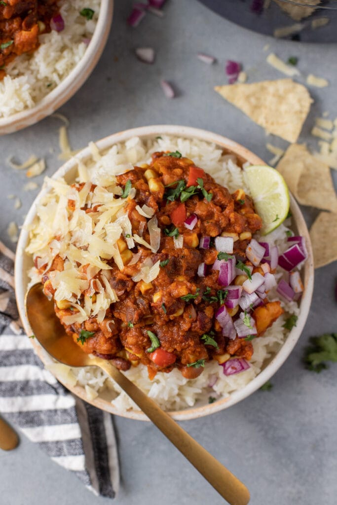 A bowl of vegan chili with a gold spoon taking a bite out of it