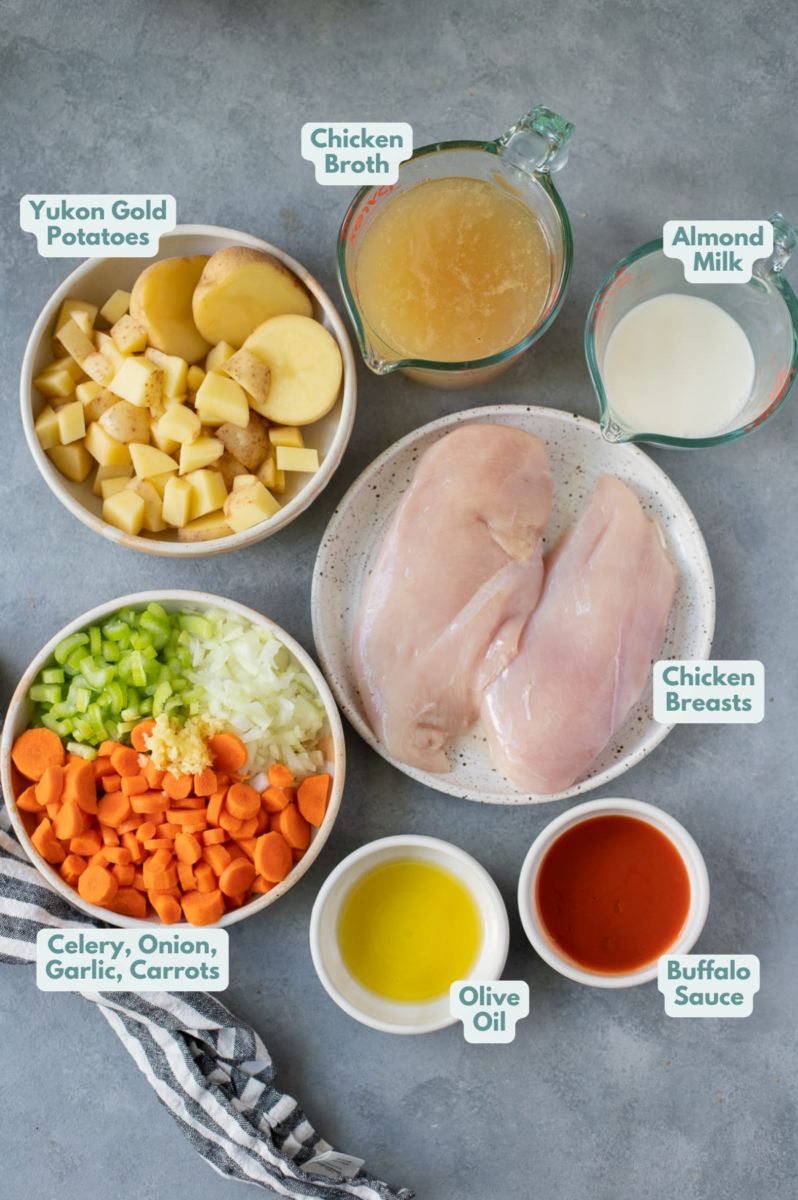 Buffalo Chicken Soup Recipe Ingredients in small white bowls on a grey background: Chicken breasts, olive oil, onion, celery, garlic, carrot, yukon gold potatoes, Frank’s Red Hot, no/low sodium chicken broth, almond milk