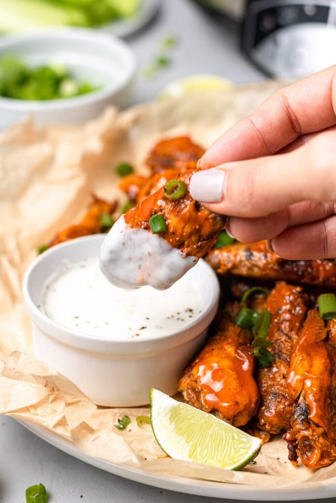 A crock pot chicken wing being dipped in ranch