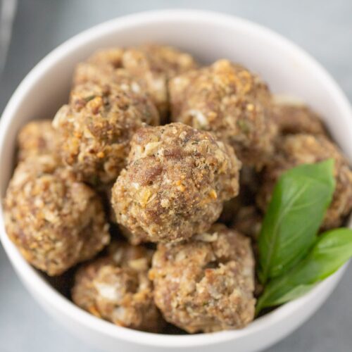A close up of a bowl of homemade meatballs on a grey background