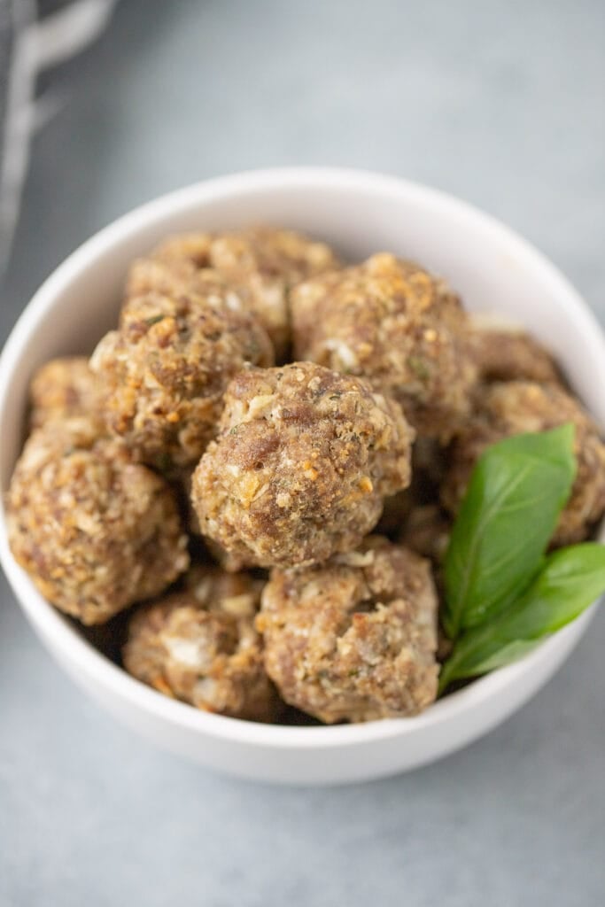 A close up of a bowl of homemade meatballs on a grey background