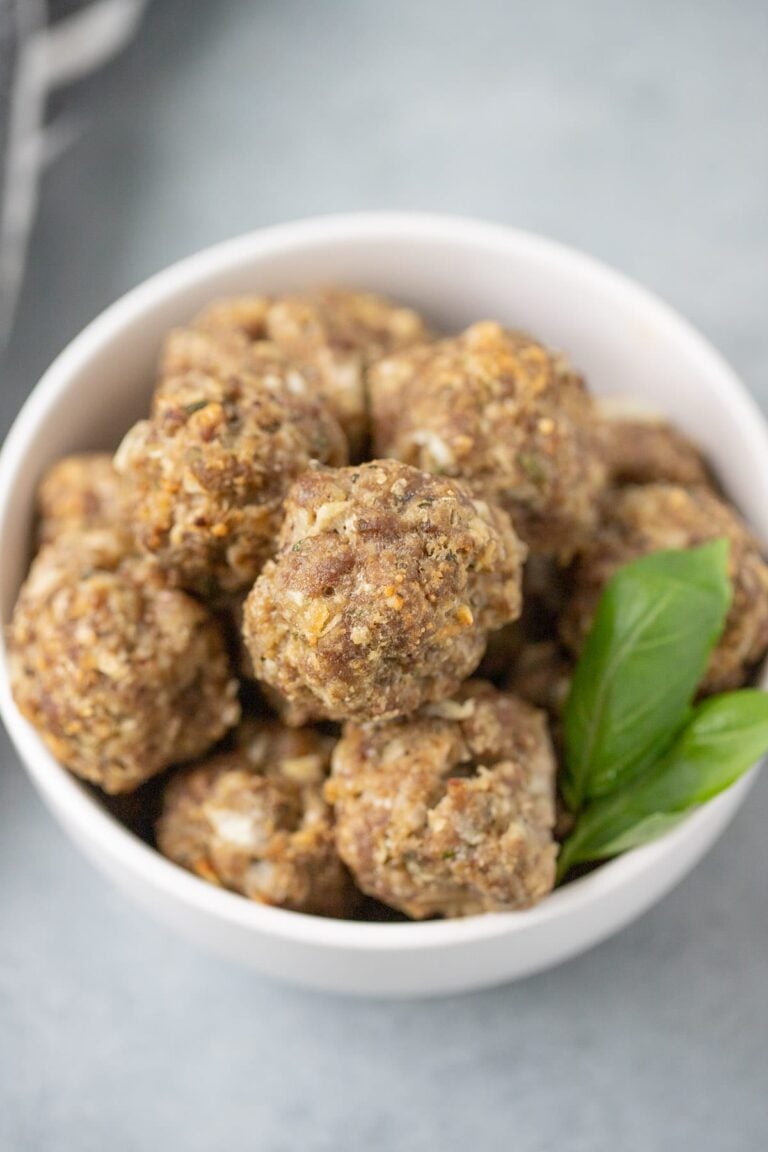 A close up of a bowl of homemade meatballs on a grey background