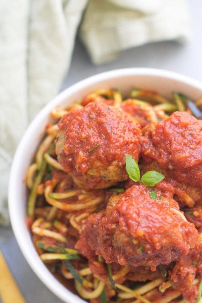 A close up of homemade meatballs covered with sauce over a bed of pasta