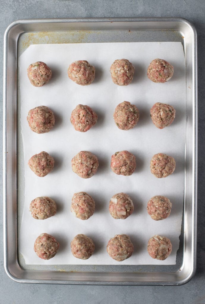 Raw meatballs on a baking sheet before being baked