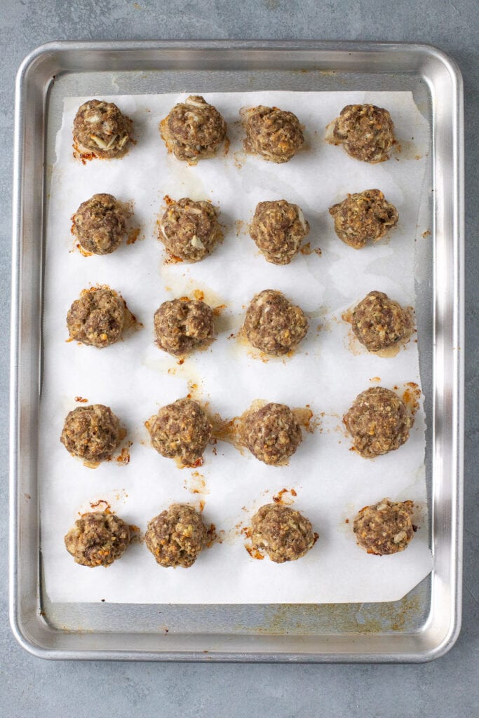 An overhead image of homemade beef meatballs on a parchment lined baking sheet