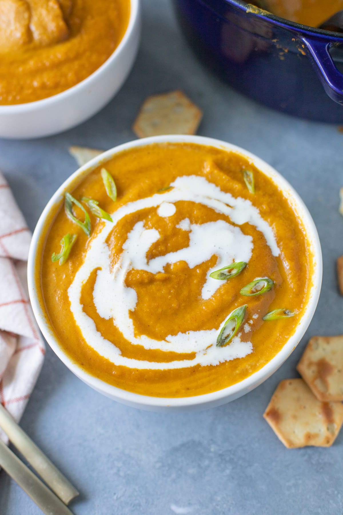Overhead view of a bowl full of thick and creamy soup made with canned pumpkin puree. The soup is garnished with chopped scallions and a drizzle of coconut cream.