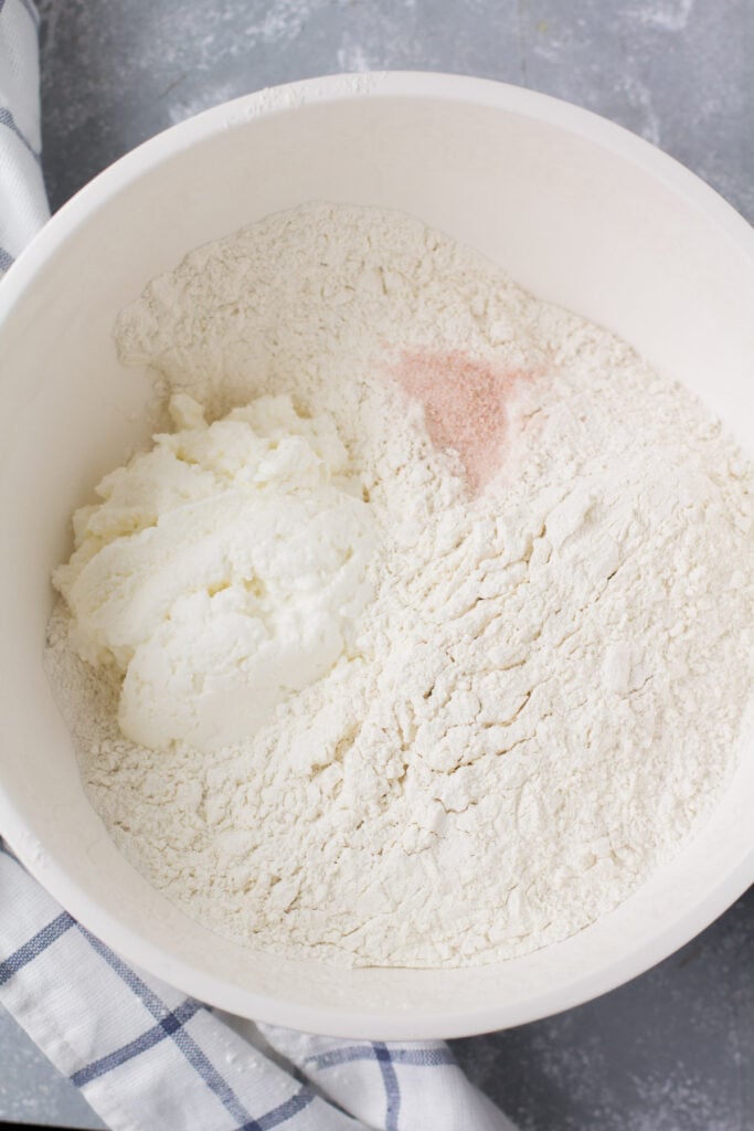 Overhead view of flour, water, and ricotta in a large white mixing bowl.