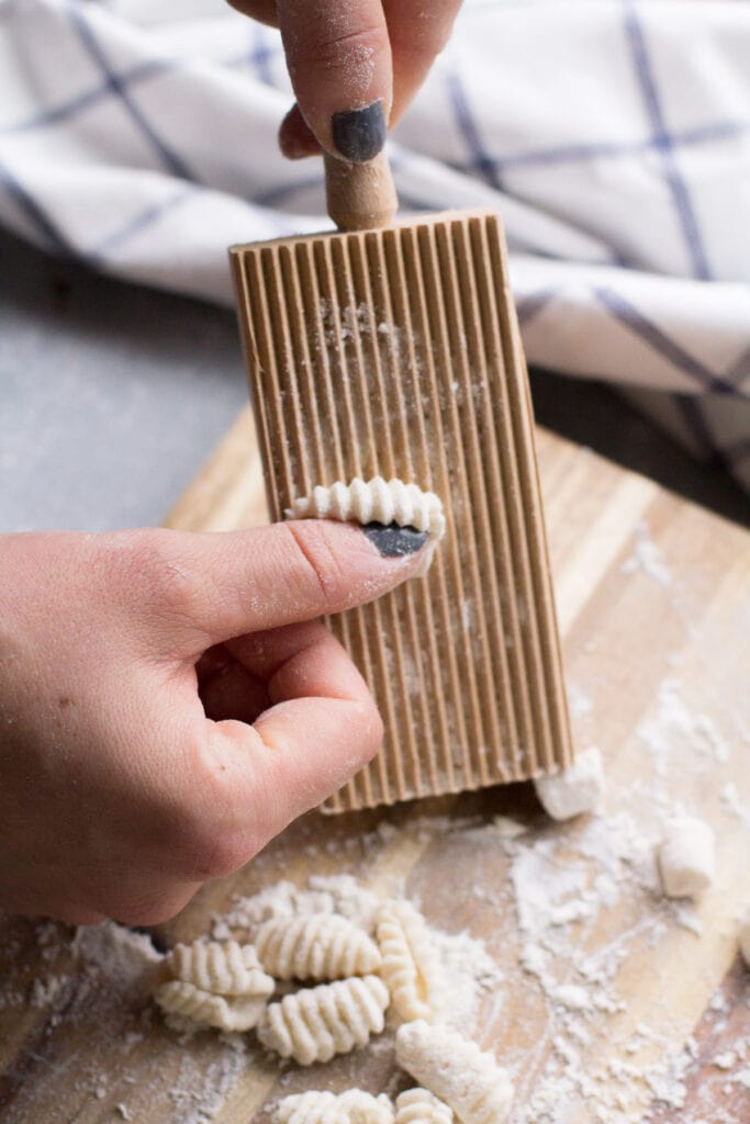 Hand rolling pieces of dough on a pasta block.