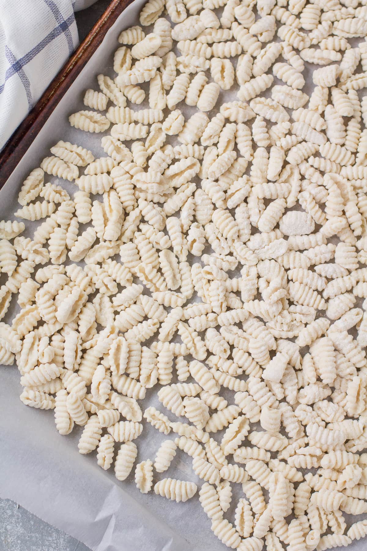 Uncooked ricotta cavatelli on a parchment lined baking sheet before being frozen.
