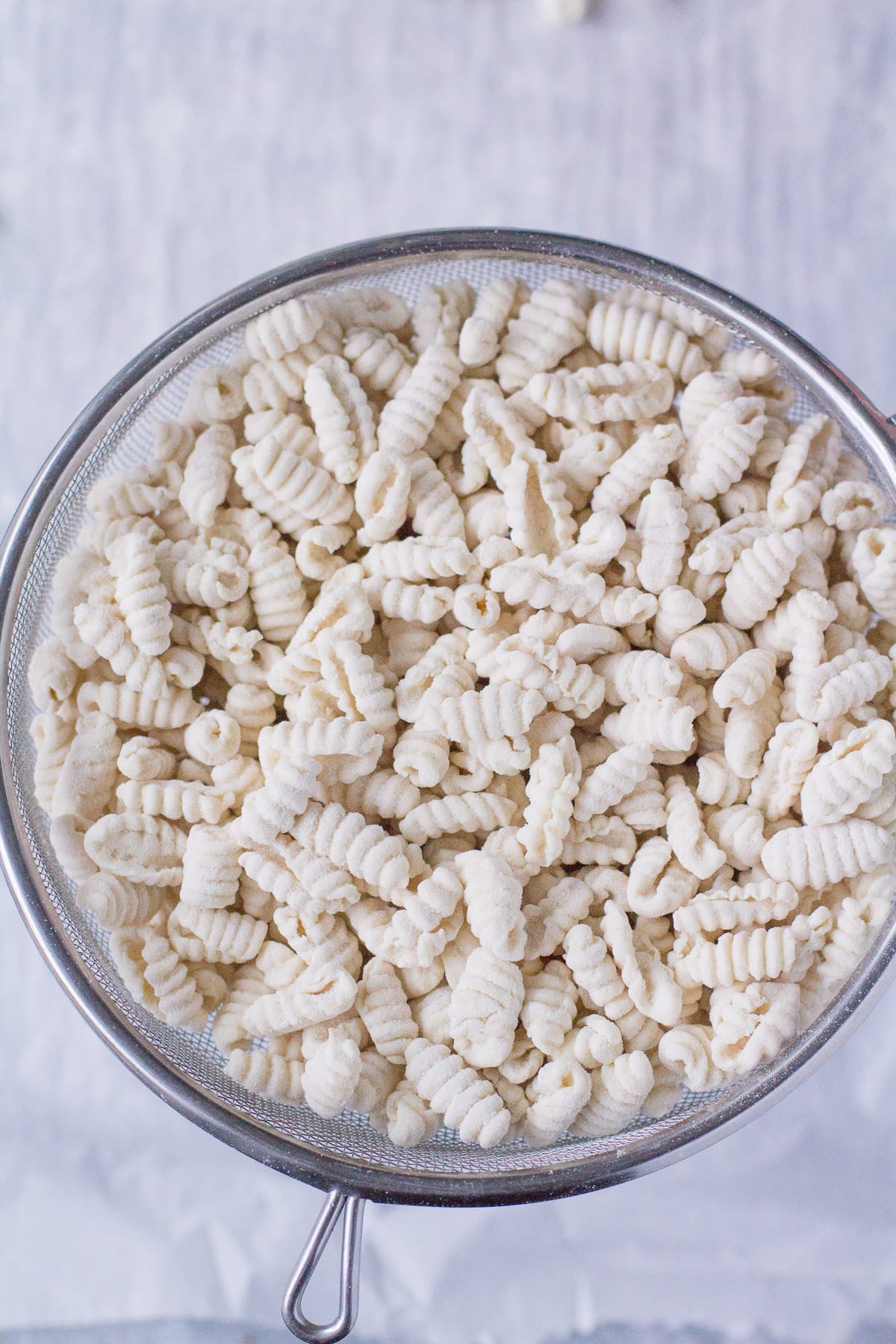 Handmade pieces of pasta in a fine mesh strainer, having the flour shaken off of them