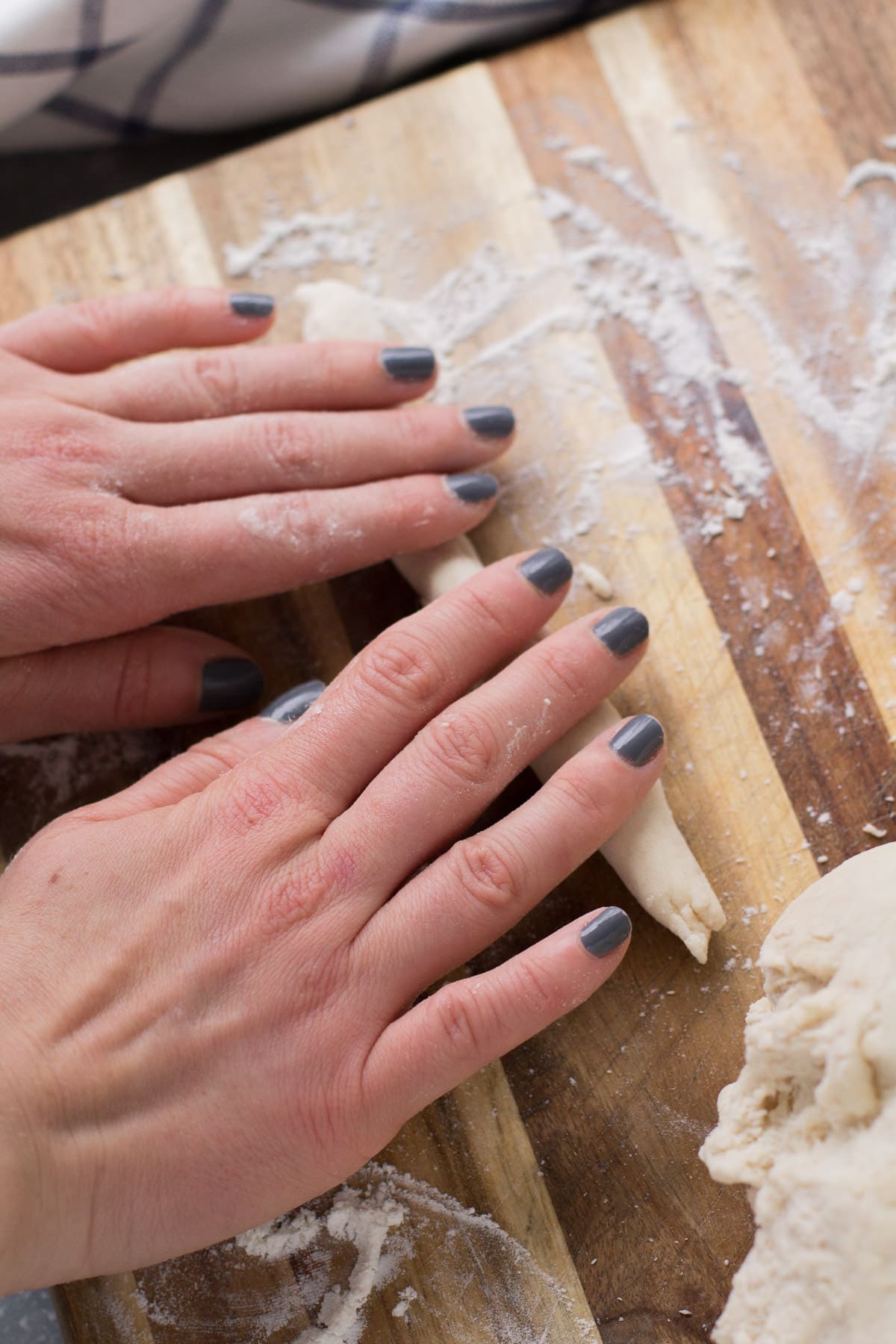 Two hands rolling pasta dough into long strips on a wooden surface.