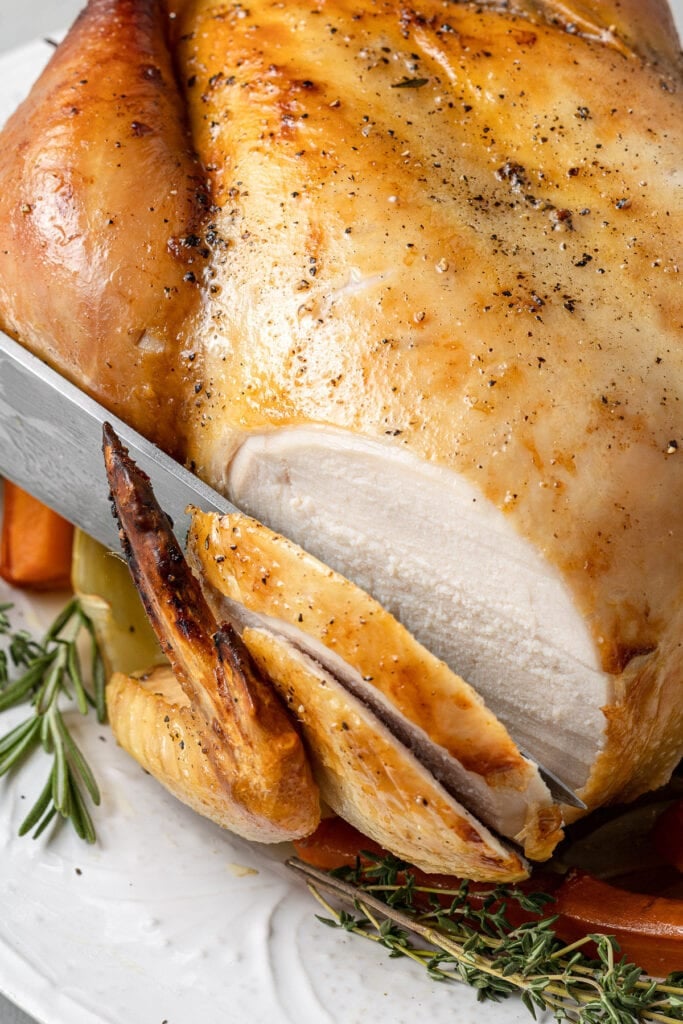 A large knife slicing into an oven roasted chicken breast