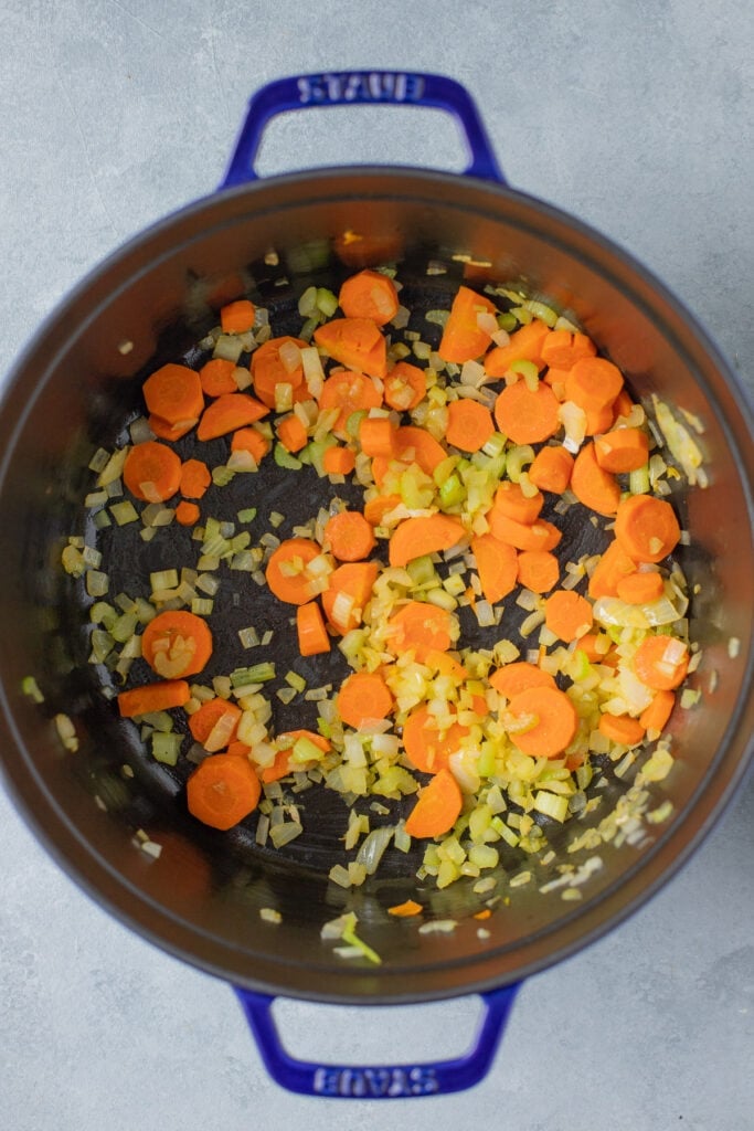 Garlic, onion, carrots, and celery sautéing in olive oil in a large pot for turkey noodle soup