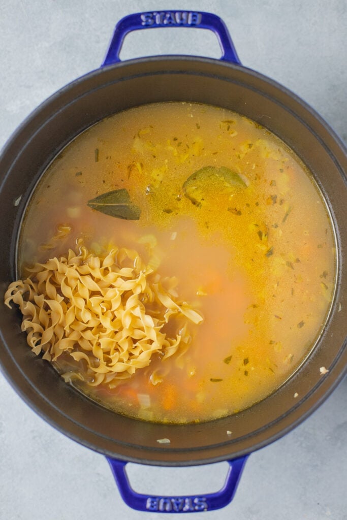 Egg noodles being added to large pot of turkey noodle soup