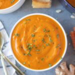 Carrot Ginger Soup with chopped parsley on top in a white bowl with a bowl of soup to the side