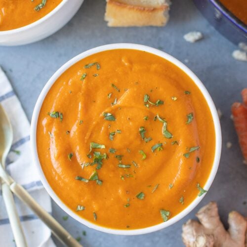 Carrot Ginger Soup with chopped parsley on top in a white bowl with a bowl of soup to the side