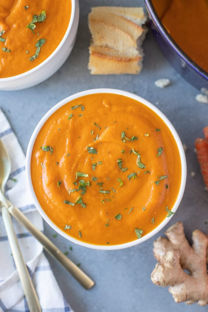 Carrot Ginger Soup Recipe with chopped parsley on top in a white bowl with a bowl of soup to the side