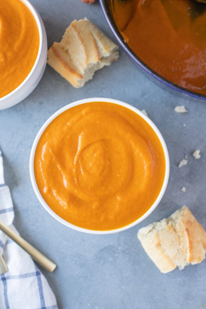 Carrot and ginger soup in a white bowl with a bowl of soup and bread to the side