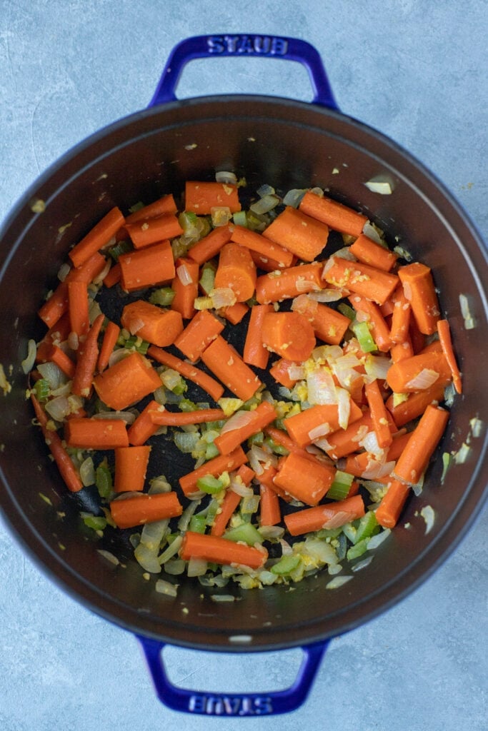 Carrots, onions, garlic, and celery sautéing in a stock pot to make carrot ginger soup