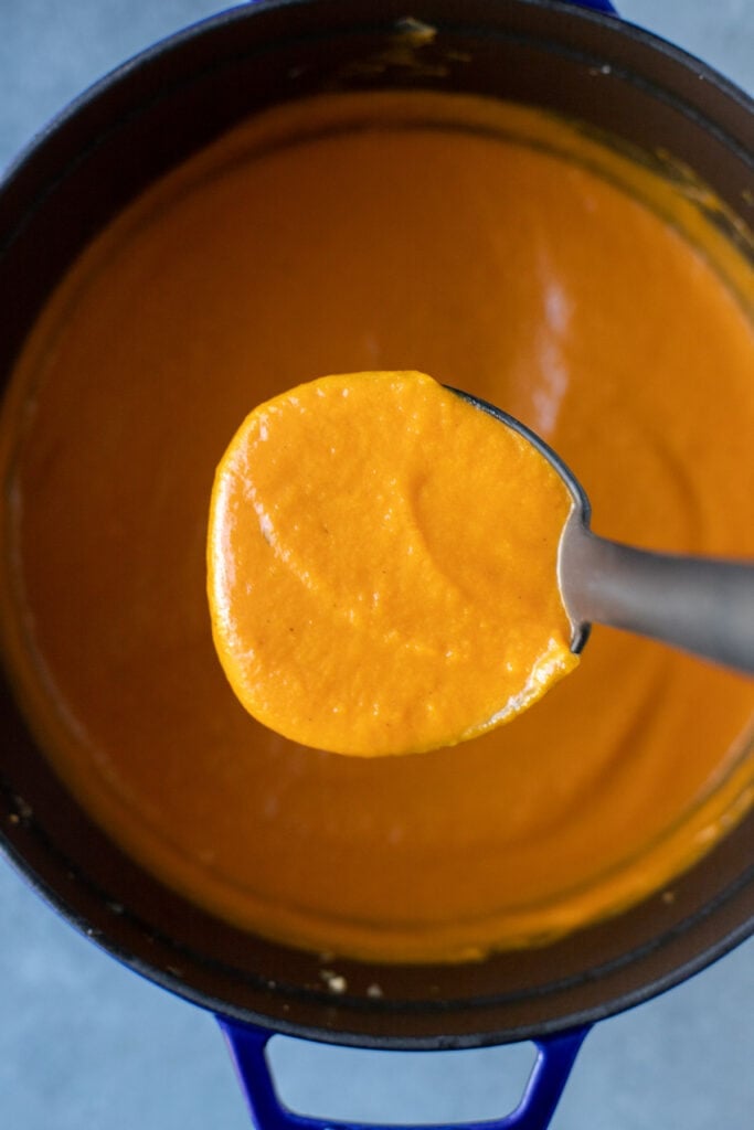 A ladle of carrot ginger hot soup being taken out of a large pot