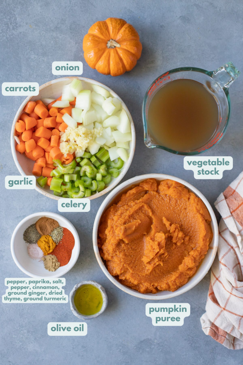 Creamy Pumpkin Bisque Recipe ingredients in small white bowls: pumpkin puree, carrots, celery, onion, olive oil, vegetable stock, garlic, honey, paprika, cinnamon, ground ginger, dried thyme, turmeric, salt & pepper