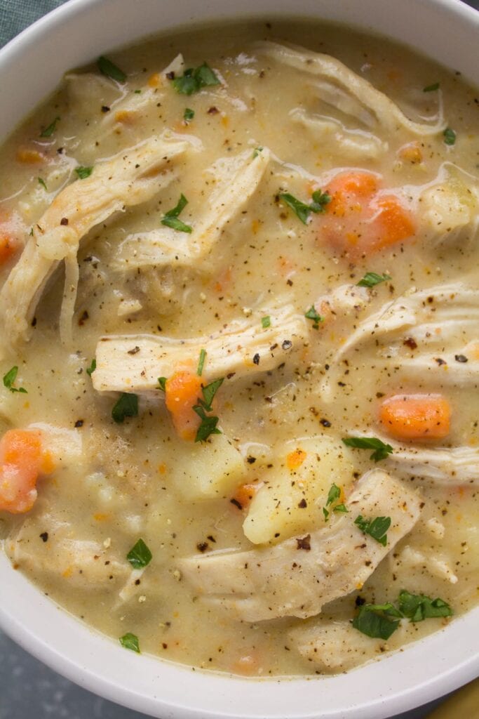 A close up of chicken pot pie soup in a white bowl - a whole30 slow cooker recipe