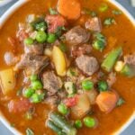 A close up of vegetable beef soup in a white bowl with a grey background