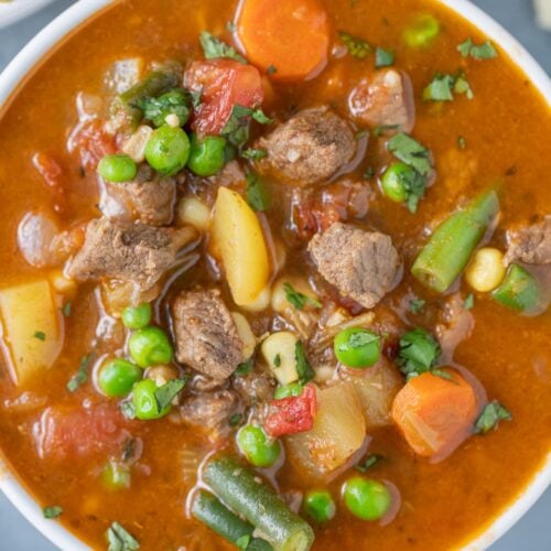 A close up of vegetable beef soup in a white bowl with a grey background