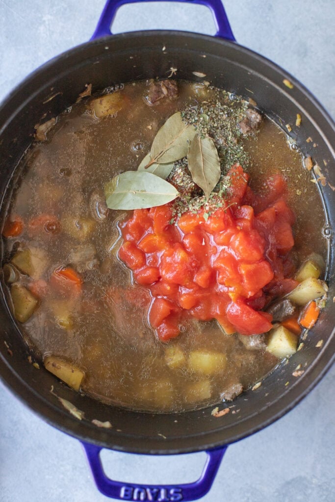 Beef stew meat, onions, garlic, carrots and celery in a stock pot with potatoes, spices, broth and canned tomatoes added