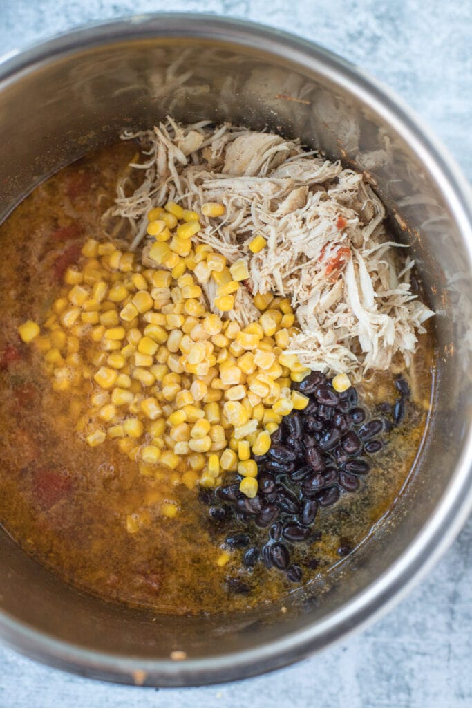 A close up of shredded chicken, corn and beans being added in to chicken tortilla soup