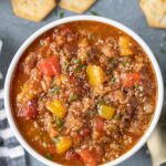A bowl of stuffed pepper soup with crackers on the side on a grey background