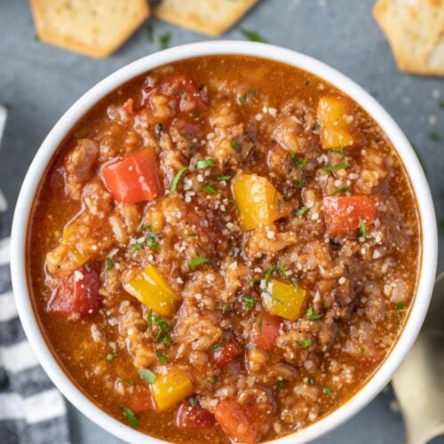 A bowl of stuffed pepper soup with crackers on the side on a grey background