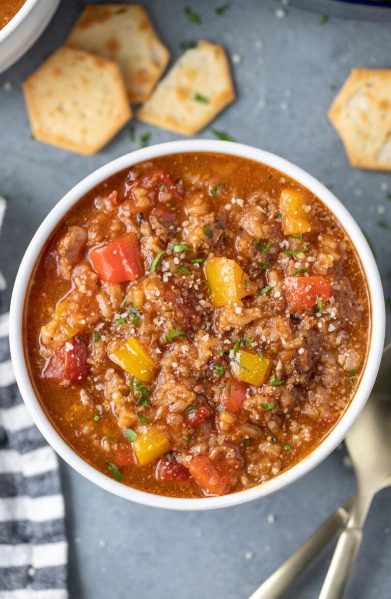 A bowl of stuffed pepper soup with crackers on the side on a grey background