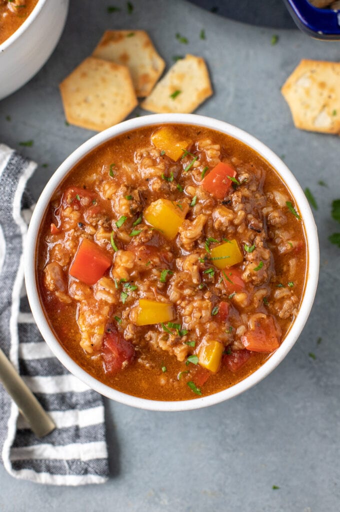 A bowl of bell pepper soup with crackers on the side on a grey background