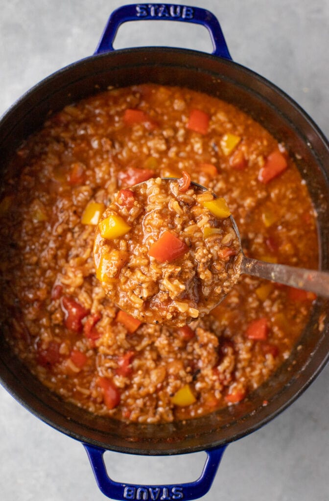 A ladle of stuffed pepper soup being taken out of a stock pot on a gray background